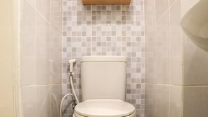 Une salle de bain avec des toilettes, des murs carrelés et une étagère en bois au-dessus des toilettes.