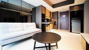 Ein modernes Wohnzimmer mit einer Couch, einem runden Tisch und einer Küchenzeile mit Kühlschrank und Schränken.