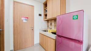 Une cuisine de taille réduite, avec des meubles de rangement en bois, un réfrigérateur rose et un évier.