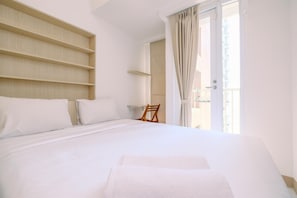 A neatly made bed with white linens, a wooden headboard, and a chair by the window. - Comfy And Best Choice Studio Apartment Tokyo Riverside Pik 2 (Teluknaga)