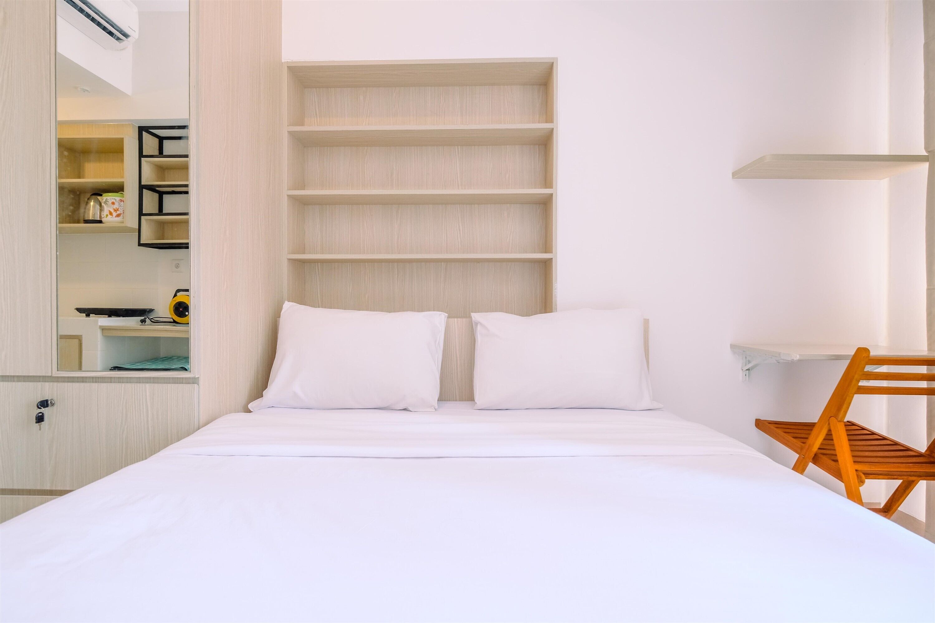 Ein Hotelzimmer mit Bett, einem Holzhocker und eingebauten Regalen mit Spiegel und Ablagefächern.