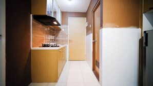 A narrow kitchen with a stove, cabinets, and a door leading to another room. - Comfy And Homey 2Br At Bale Hinggil Apartment (Surabaya)