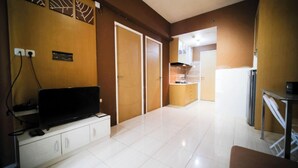 A modern kitchen with a refrigerator, microwave, and stove. There is a TV on a stand and a cabinet with drawers. The floor is tiled, and the walls are painted in a warm color. - Comfy And Homey 2Br At Bale Hinggil Apartment (Surabaya)