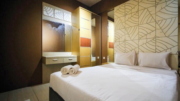 A hotel room with a large bed, a wardrobe, a mirror, and a decorative wall panel. - Comfy And Homey 2Br At Bale Hinggil Apartment (Surabaya)
