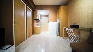 A hallway with a kitchen area, a refrigerator, and a dining table with chairs. - Comfy And Homey 2Br At Bale Hinggil Apartment (Surabaya)