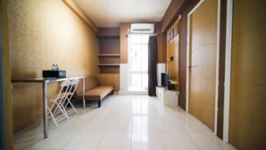 A compact hotel room with a kitchenette, a sofa, a desk with chairs, and a large window with curtains. - Comfy And Homey 2Br At Bale Hinggil Apartment (Surabaya)