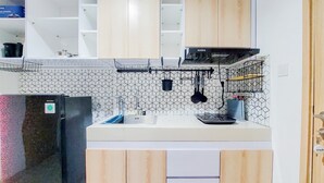A kitchen with white cabinets, a black refrigerator, a tiled backsplash, and hanging utensils. - Comfort 1Br Without Living Room Bintaro Embarcadero Apartment (South Tangerang)