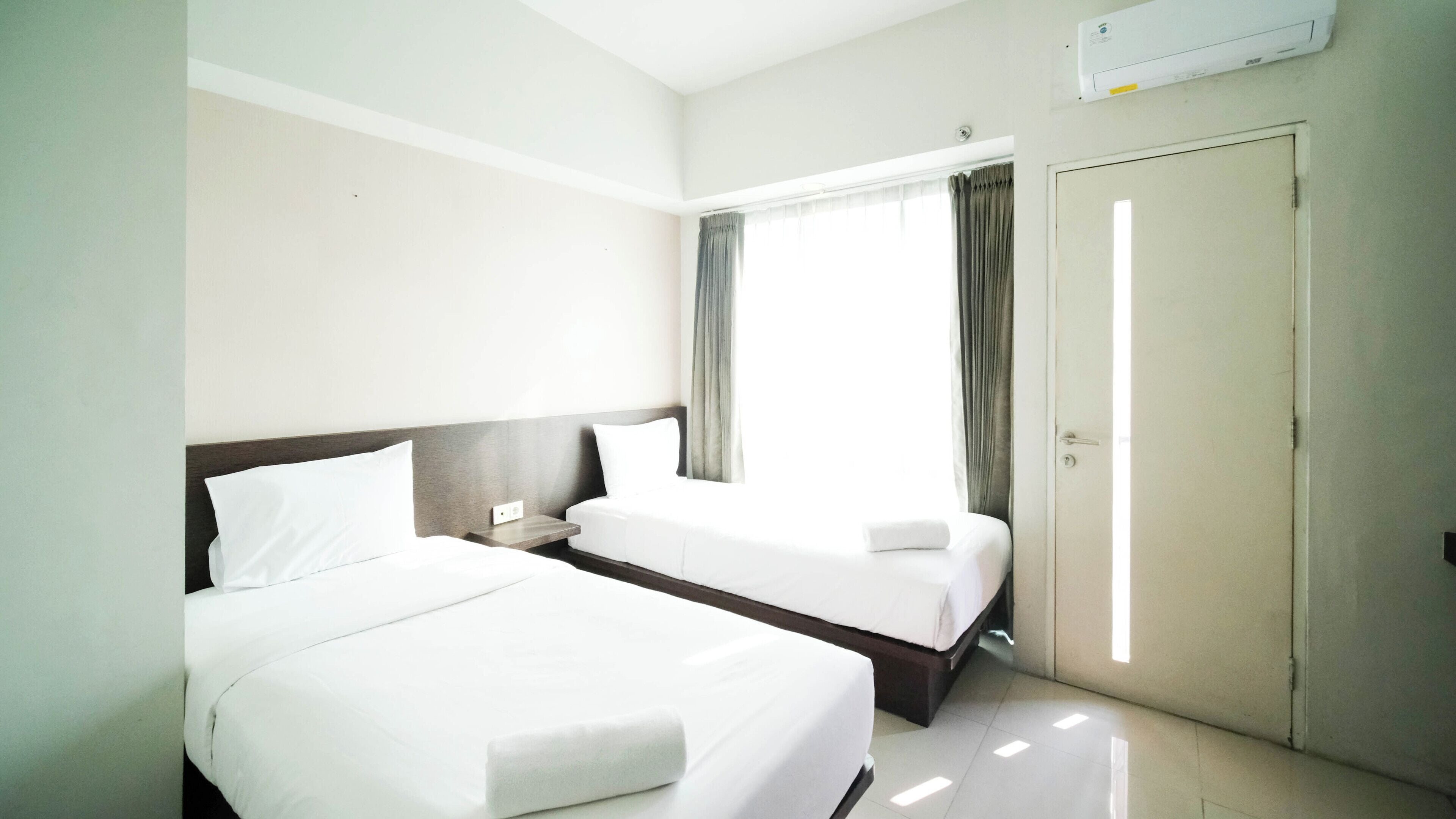 Ein Hotelzimmer mit zwei Betten, einem Fenster mit Vorhängen, einer Klimaanlage und einer Tür.