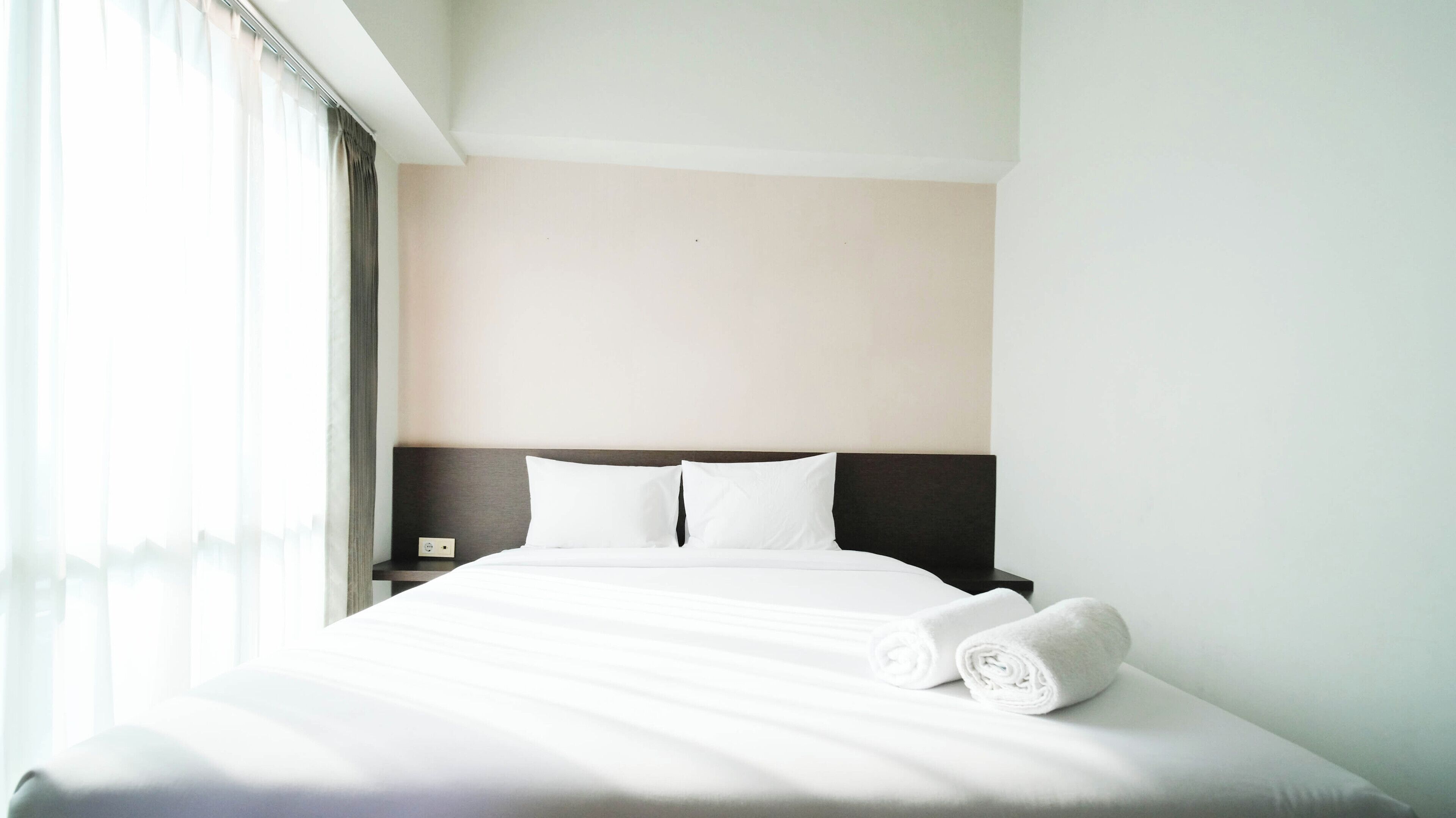 A hotel room with a neatly made bed, a nightstand, and a window with curtains.