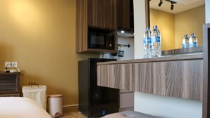 A hotel room with a bed, a small seating area, a microwave, a trash bin, and a minibar with water bottles. - Simply Look Studio Room LRT City Jatibening Apartment (Bekasi)