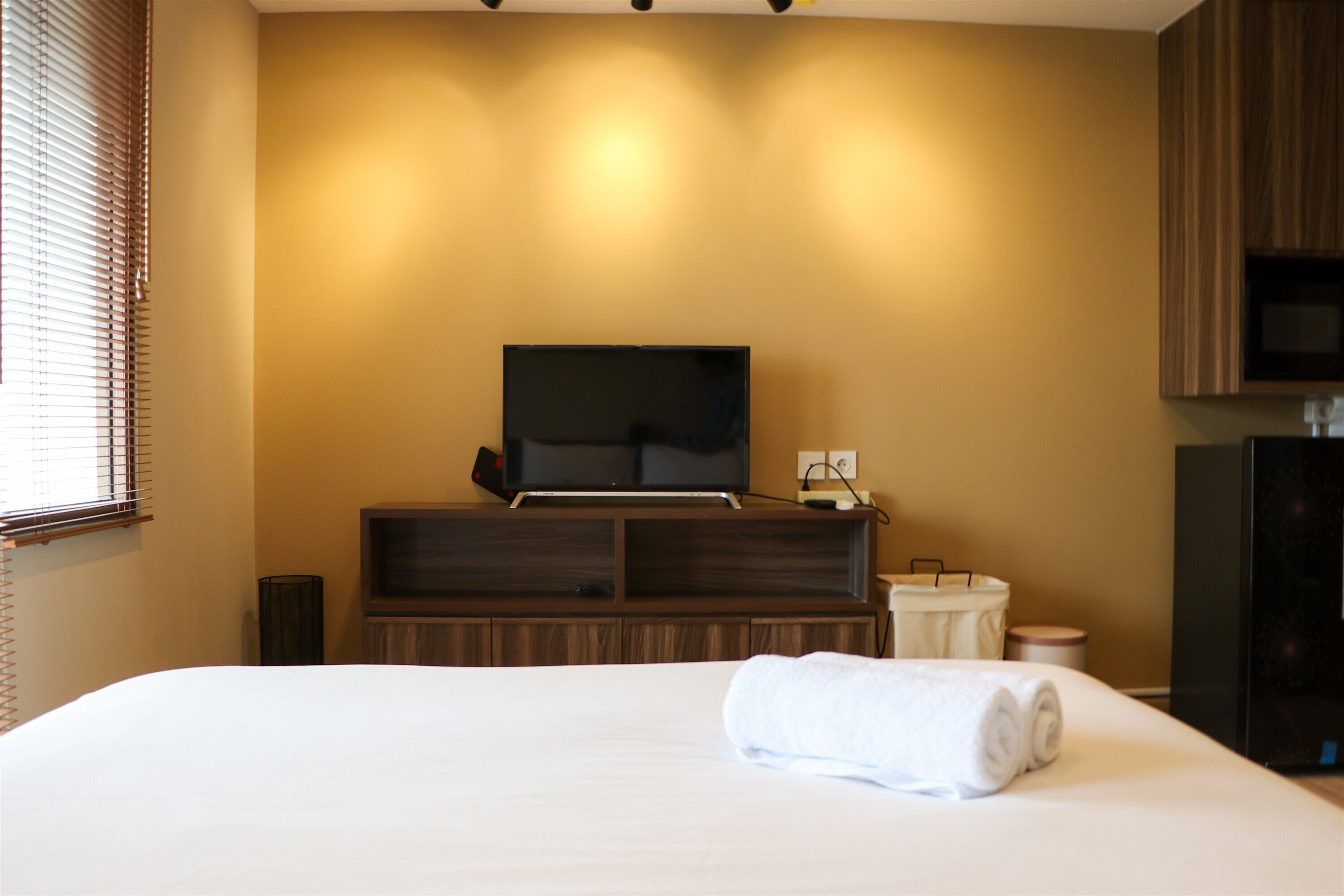 A hotel room with a large bed, a flat-screen TV, wooden cabinets, and a small table with a lamp.