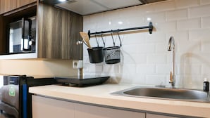 A modern kitchen with a stainless steel sink, a microwave, and a black hanging rack with kitchen utensils. - Simply Look Studio Room LRT City Jatibening Apartment (Bekasi)