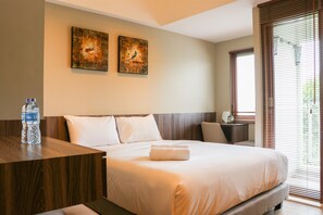 Ein Hotelzimmer mit einem großen Bett, zwei an der Wand befestigten Kunstwerken, einem Nachttisch aus Holz mit einer Wasserflasche und einem Fenster mit Jalousien.