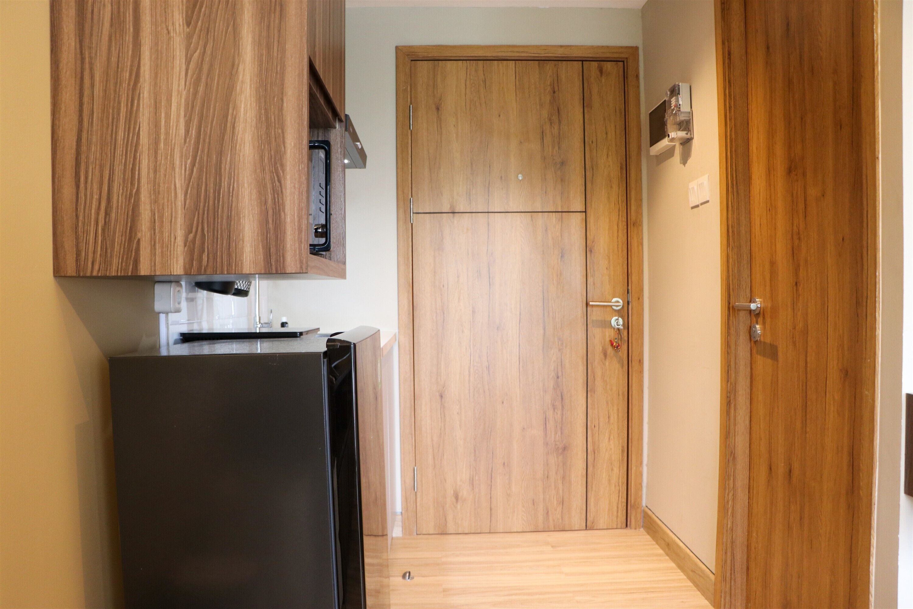 A compact kitchen with a black refrigerator, wooden cabinets, and a wooden door.
