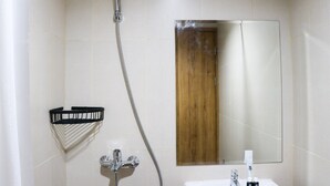 A bathroom with a shower, a sink, a mirror, and a wooden panel. - Simply Look Studio Room LRT City Jatibening Apartment (Bekasi)