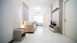 A modern living room with a sofa, TV stand, and a window with a view. - Cozy And Homey 2Br At Benson Supermall Mansion Apartment (Surabaya)