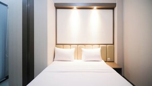 A hotel room with a bed, two pillows, a headboard with integrated lighting, and a bedside table. - Cozy And Homey 2Br At Benson Supermall Mansion Apartment (Surabaya)