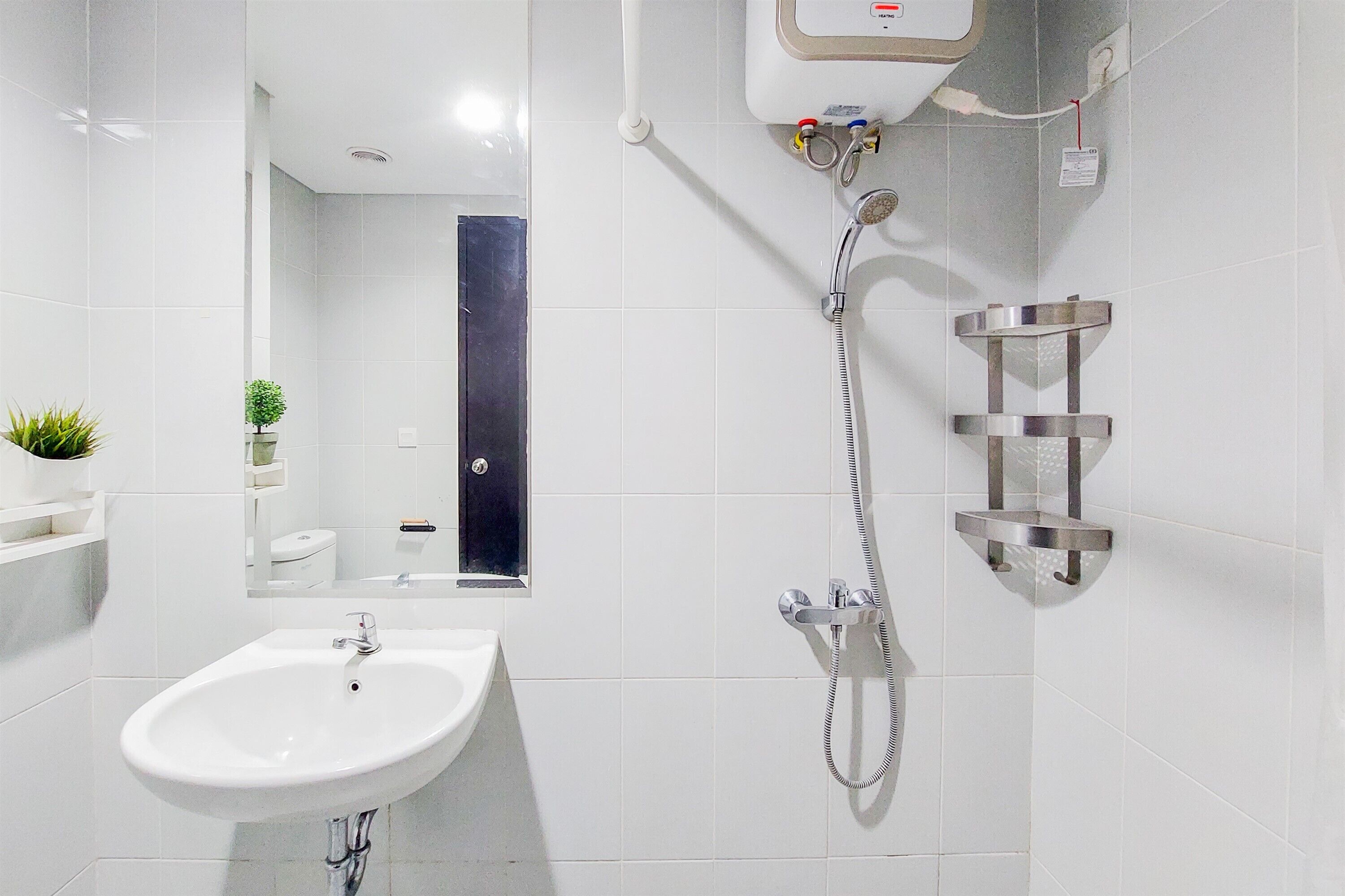 Un bagno moderno con un lavandino bianco, uno specchio, una doccia con soffione a mano e un erogatore di sapone montato a parete.