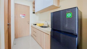 A kitchen with wooden cabinets, a black refrigerator, a sink, and a door with a fire safety sign. - Cozy Stay And Good Deal Studio Apartment B Residence (Pagedangan)