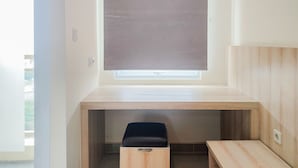 A small, modern room with a built-in desk, a window with a blind, and a small stool. - Cozy Stay And Good Deal Studio Apartment B Residence (Pagedangan)