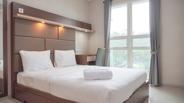 A modern hotel room with a large bed, a wooden headboard, a desk, and a window with curtains. - 2Br Citralake Suites 2Nd Floor Comfy Easy Access Apartment (Jakarta)