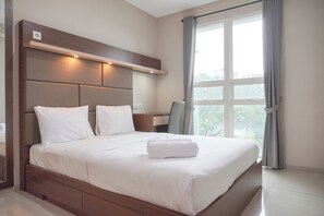 Ein modernes Hotelzimmer mit einem großen Bett, einem Holz-Kopfteil, einem Schreibtisch und einem Fenster mit Vorhängen.