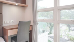 A hotel room with a wooden desk, a chair, a bed, and a window with a view of the outside. - 2Br Citralake Suites 2Nd Floor Comfy Easy Access Apartment (Jakarta)