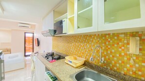 A compact kitchen with a microwave, sink, and a colorful mosaic backsplash.