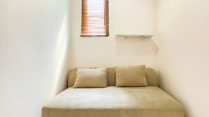 A small, single-bed room with a beige sofa and two pillows.