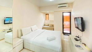 A hotel room with a bed, a desk with a TV, a mirror, and an air conditioning unit.