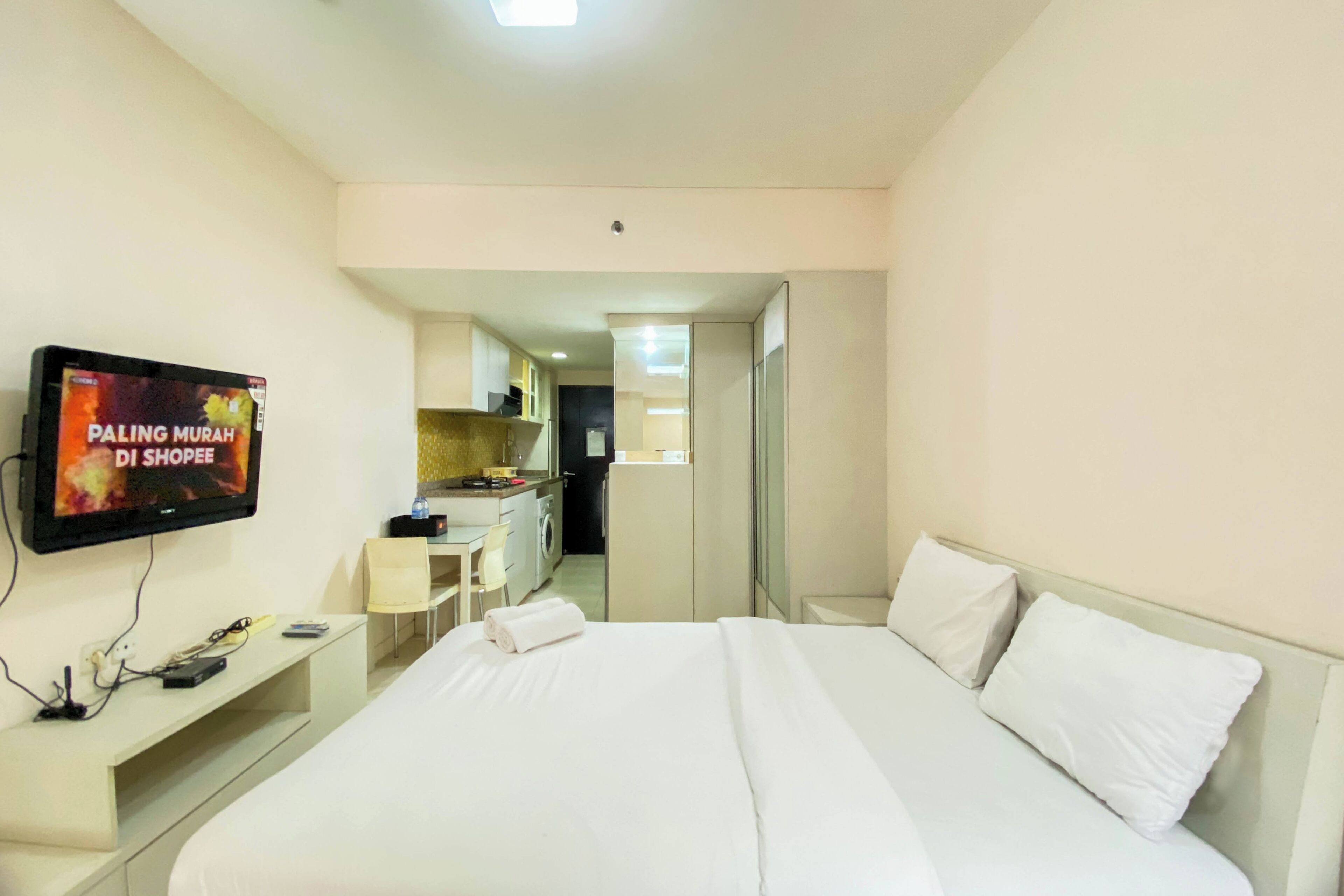 A hotel room with a bed, a TV mounted on the wall, a desk, and a mirror.