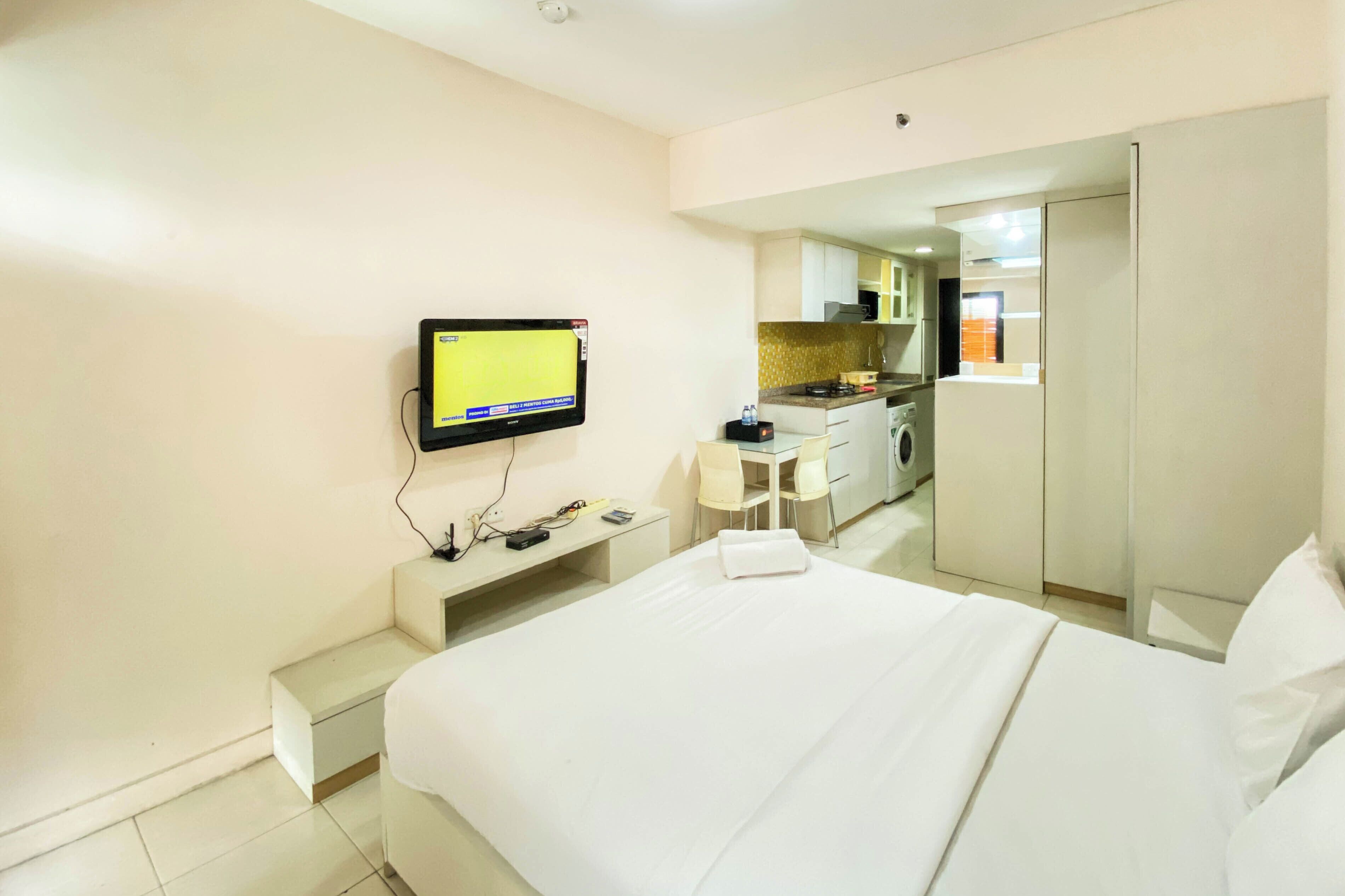 A hotel room with a bed, a desk, a chair, a television, and a kitchenette.