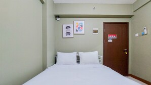 A hotel room with a bed, white bedding, a door, and two framed pictures on the wall. - Comfy And Modern Studio (No Kitchen) At Loftvilles City Apartment (South Tangerang)