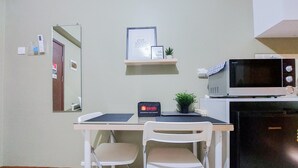 A compact kitchen with a microwave, refrigerator, and a small shelf with framed pictures. There is a chair and a desk with a computer. - Comfy And Modern Studio (No Kitchen) At Loftvilles City Apartment (South Tangerang)