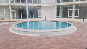 A swimming pool with a brick border, surrounded by a building with large windows. - Modern Classic Studio At Majestic Point Serpong Apartment (Gading Serpong)