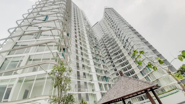 A high-rise building with a modern architectural design, featuring a curved facade and numerous windows. - Modern Classic Studio At Majestic Point Serpong Apartment (Gading Serpong)