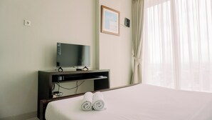 A hotel room with a bed, a TV on a stand, a framed picture on the wall, and a window with curtains. - Modern Classic Studio At Majestic Point Serpong Apartment (Gading Serpong)