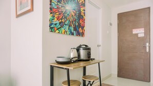 A small kitchen area with a table, two stools, a coffee maker, and a kettle. - Modern Classic Studio At Majestic Point Serpong Apartment (Gading Serpong)