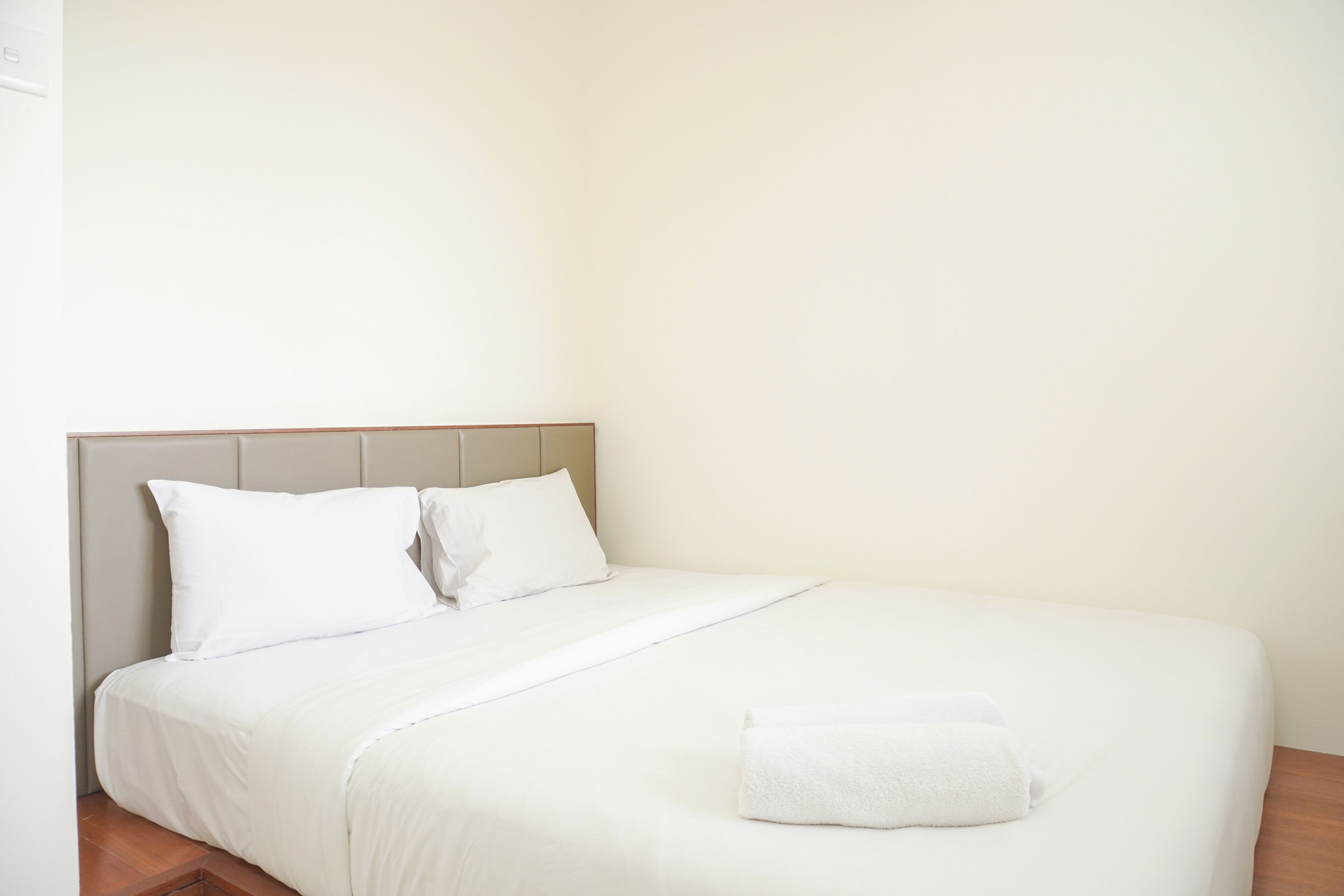 A neatly made bed with white linens and a folded towel on the side.