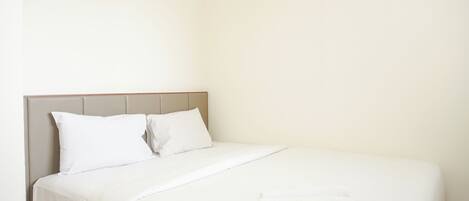 A neatly made bed with white linens and a folded towel on the side.