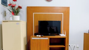 Un espacio habitable compacto con un mueble de madera que alberga un televisor de pantalla plana, un refrigerador pequeño y una planta en maceta.