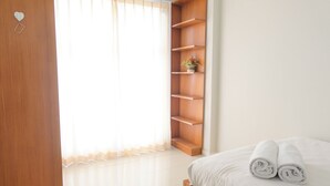 Un dormitorio con cama, una estantería de madera y una ventana con cortinas de gasa.