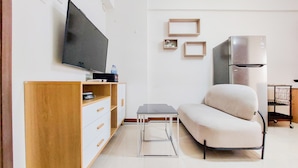 Una sala de estar moderna con televisor de pantalla plana, un sofá, una mesita y un refrigerador.
