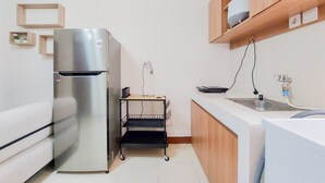 Una cocina compacta con un refrigerador de acero inoxidable, un mueble de madera sobre el lavamanos y un estante con una flor.