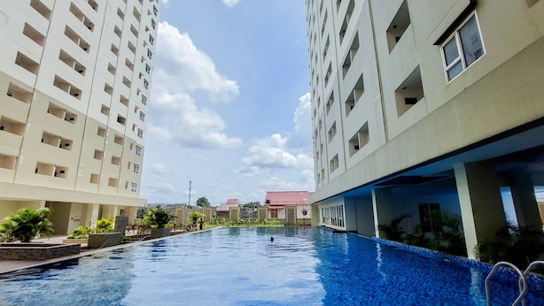 Una piscina rodeada de edificios altos con balcones, cielo despejado y una vista distante de un edificio de tejados rojos.