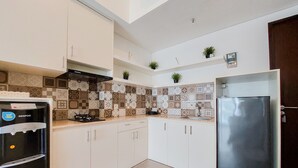 A kitchen with white cabinets, a black refrigerator, a stainless steel refrigerator, a water dispenser, and a tiled backsplash. - Strategic And Restful 1Br At Casa De Parco Apartment (South Tangerang)