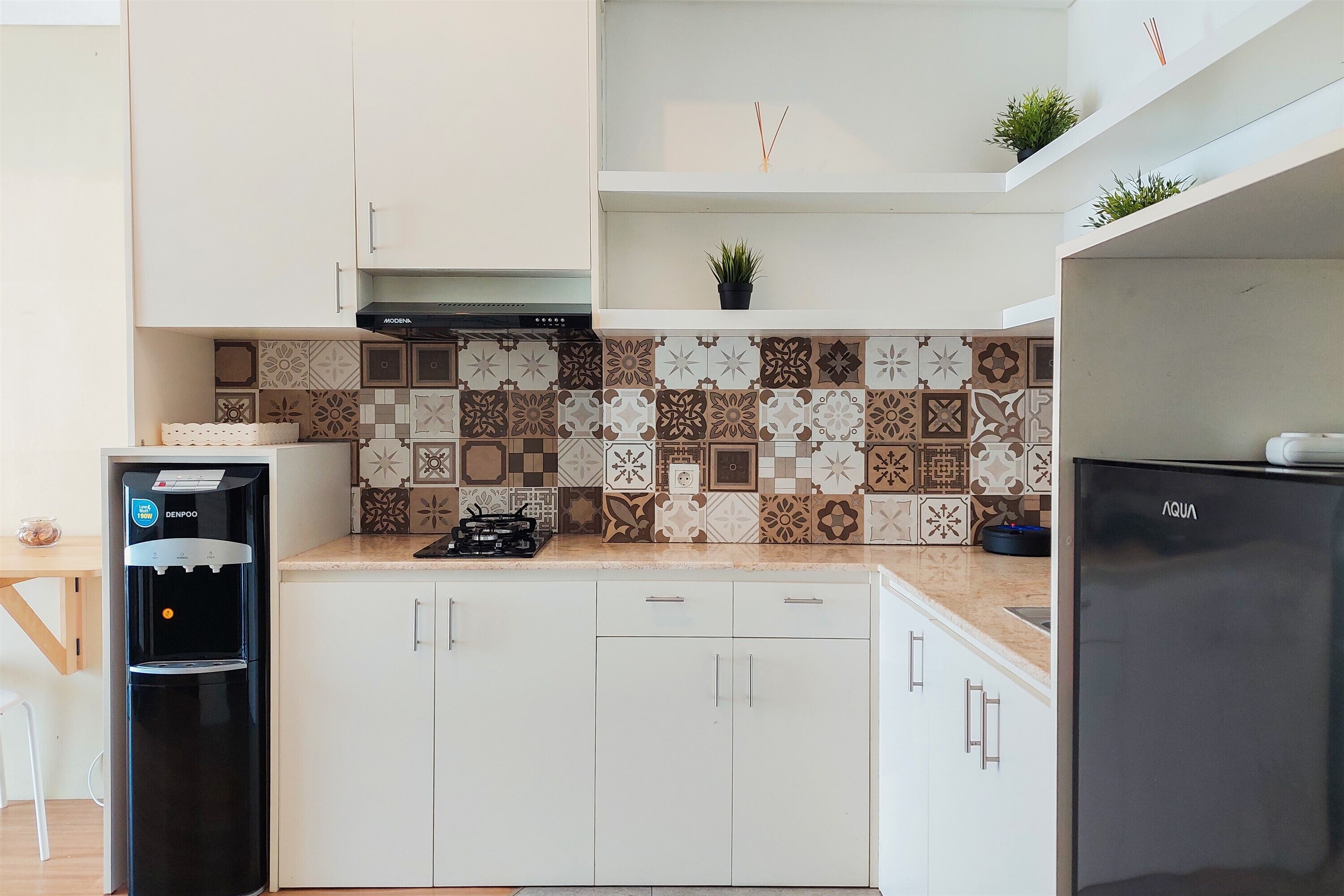 Une cuisine moderne avec des meubles blancs, un distributeur d’eau noir, une cuisinière à gaz et un réfrigérateur noir.