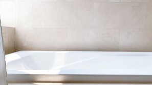 A white bathtub in a bathroom with beige tiled walls.