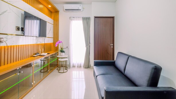 Una sala de estar moderna con un sofá negro, un tocador de madera con un espejo, una mesita redonda con una planta en maceta y una puerta con panel de madera.