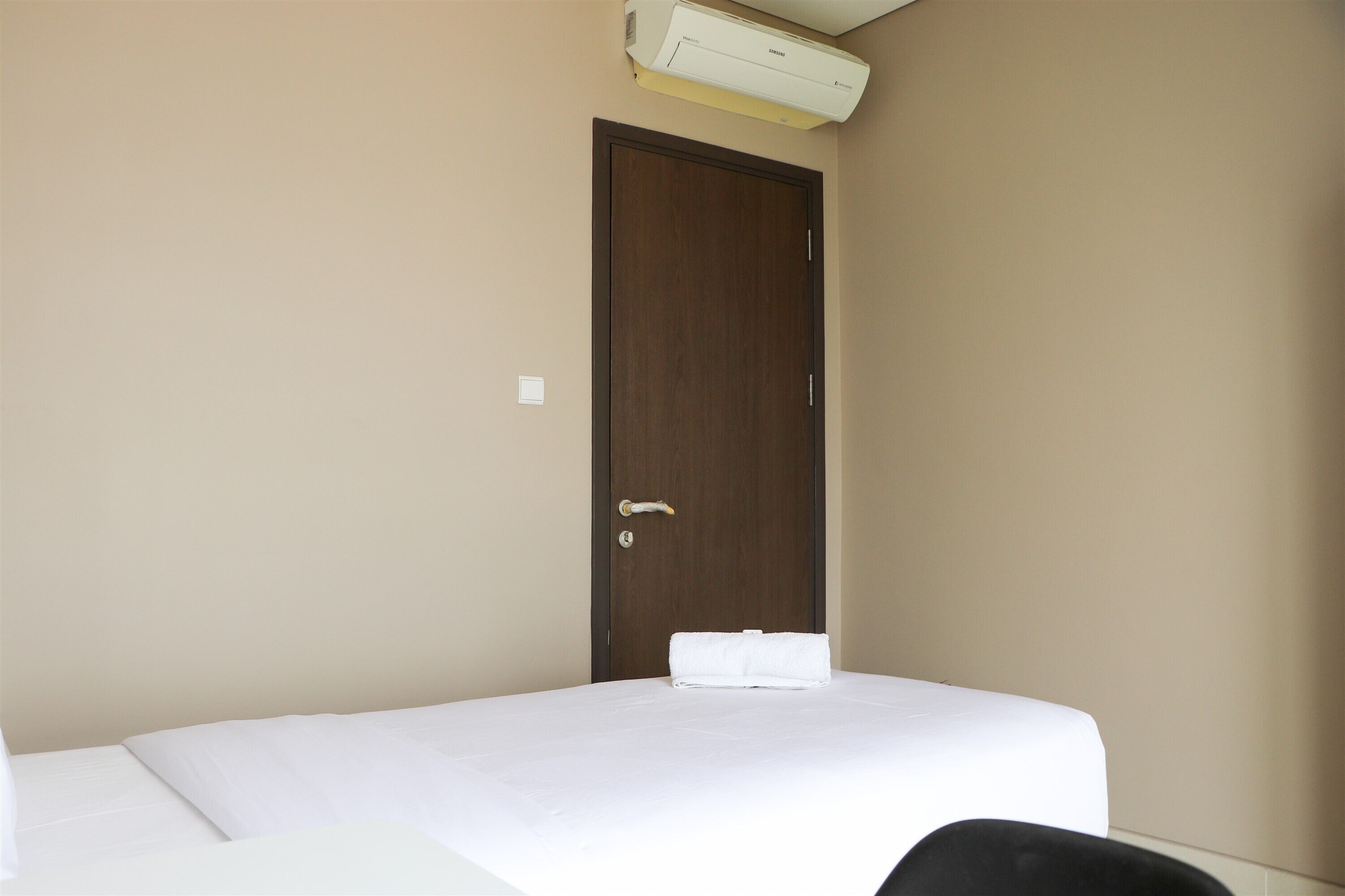 A hotel room with a single bed, a wooden door, and an air conditioning unit above it.